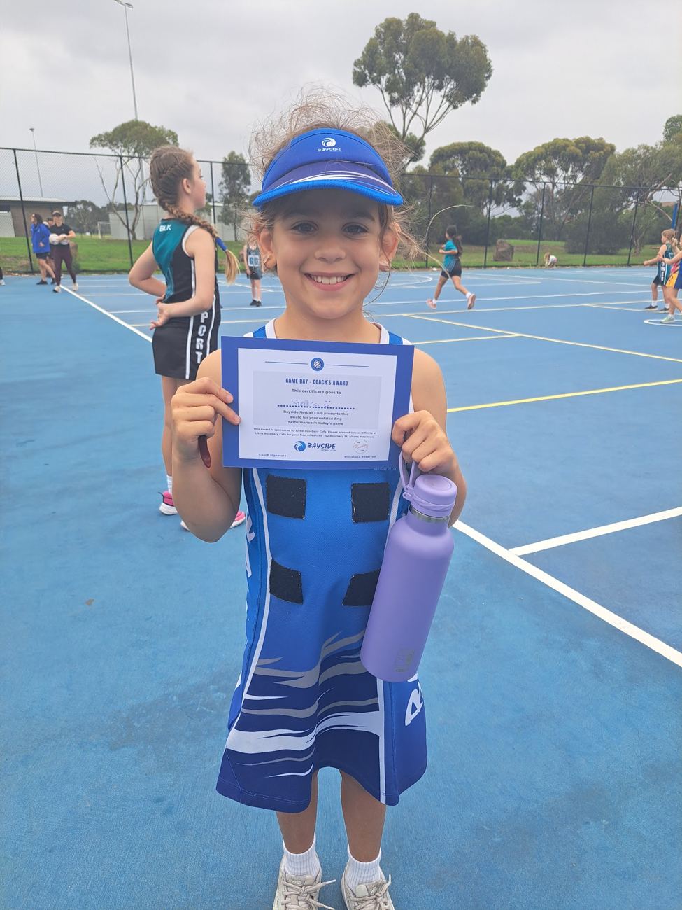 A young Net Set Go player holding her certificate on court